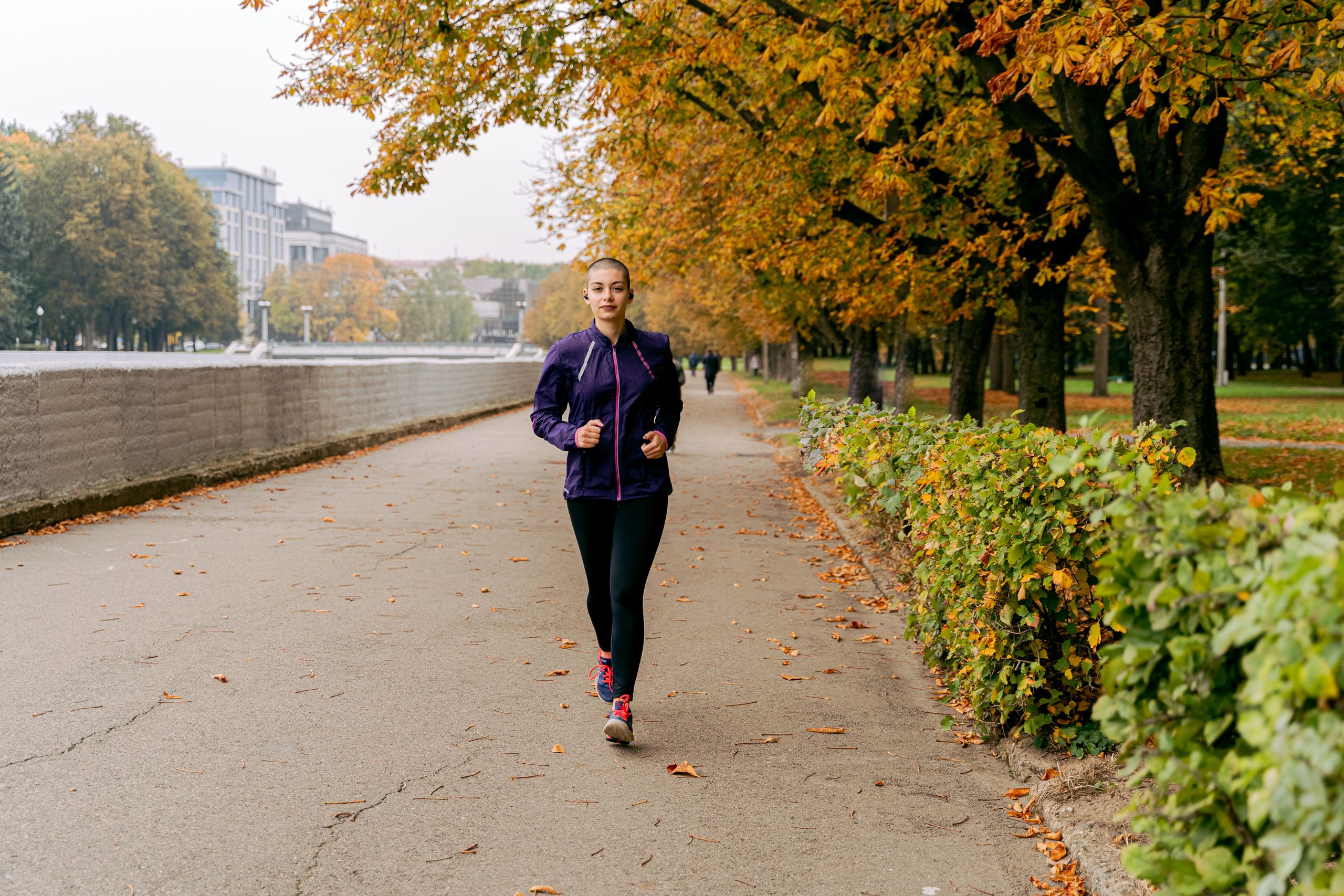 Woman jogging on a tree-lined path in the park with autumn leaves.